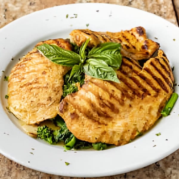 Grilled chicken cutlets with grill marks, served over green broccoli rabe and garnished with fresh basil.