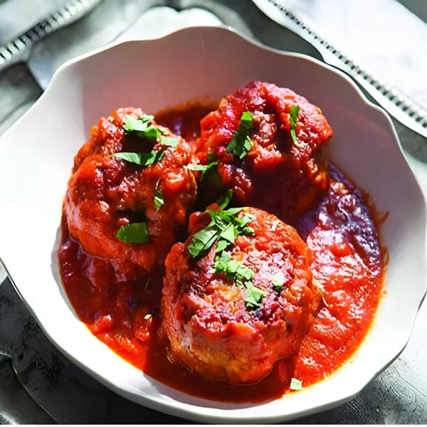 Three large meatballs covered in red sauce and fresh green herbs in a white bowl.