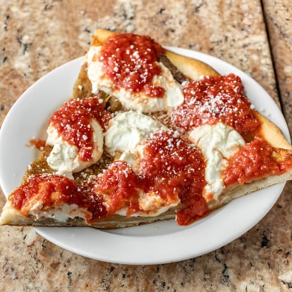 Two slices of Phil's Pizzeria pizza with dollops of ricotta cheese and red sauce on a white plate.